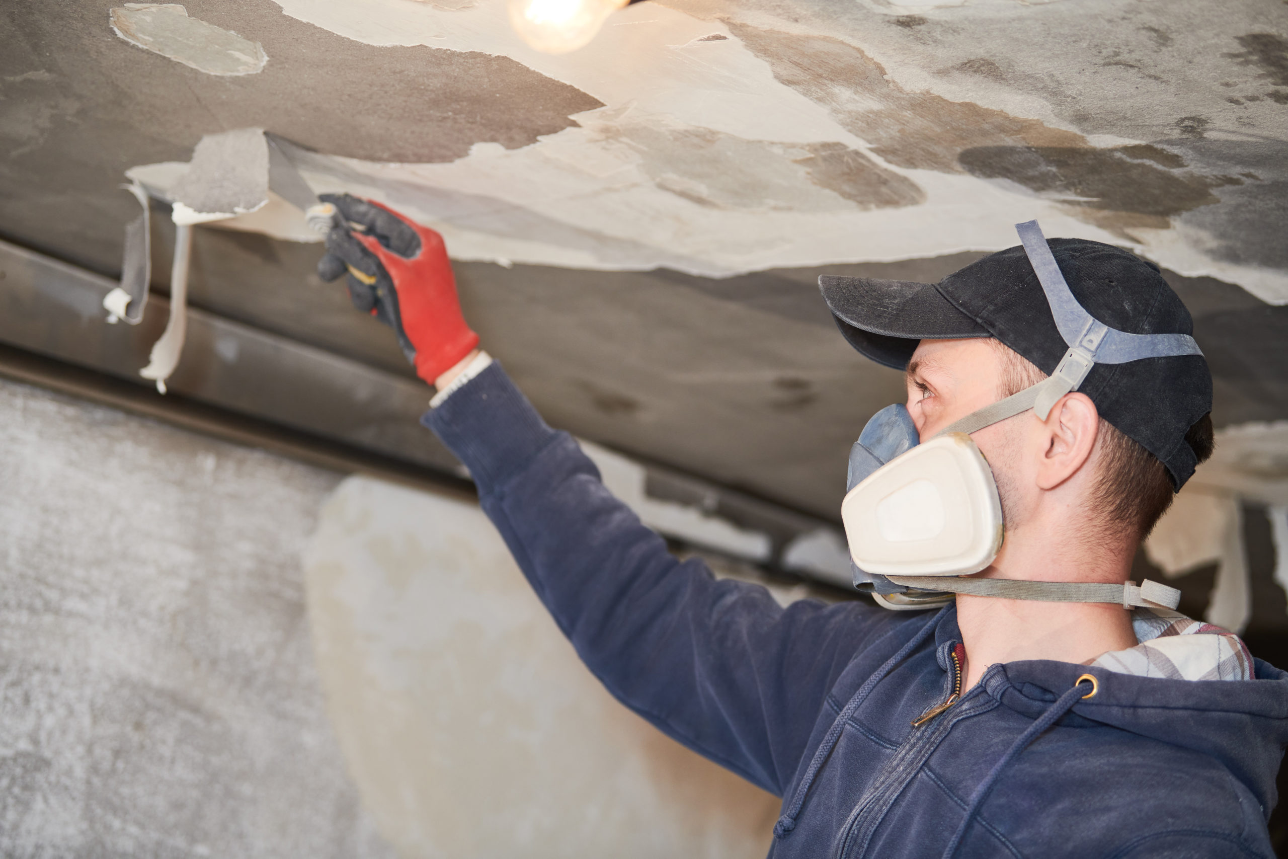 restoration and renovation after fire. Worker removes damaged paint layer from wall and ceiling indoors.
